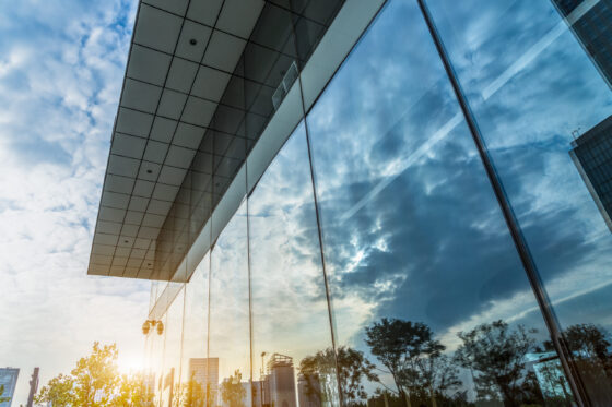 Modern glass building reflecting cloudy blue sky
